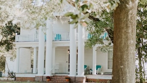 A white colonial-style building with a porch, columns, and a brick foundation.