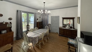 A dining room with a round table, chairs, a chandelier, and a view of the outdoors through a window.