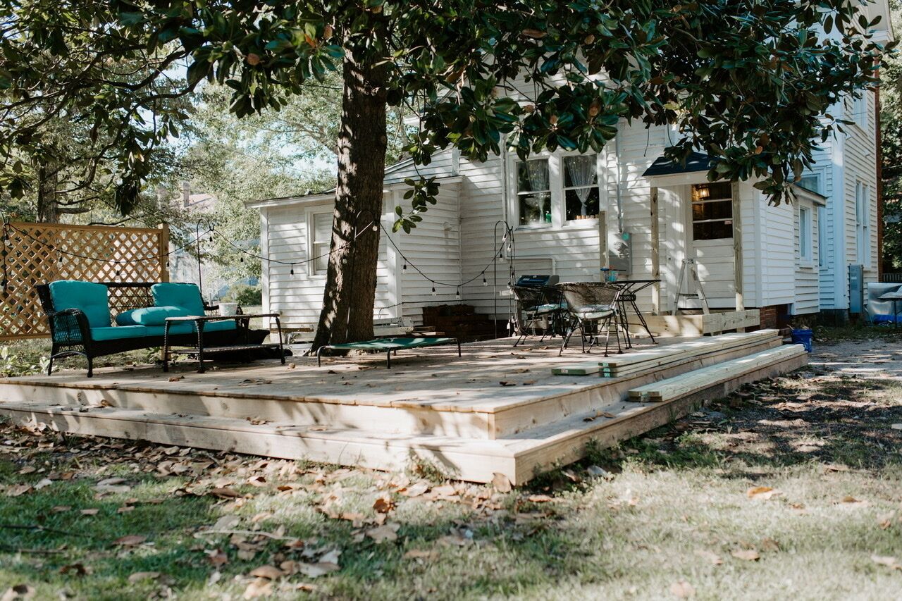 Una casa blanca con un porche, una silla verde, una mesa y un árbol.