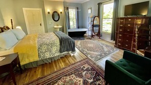 A bedroom with a bed, a vanity, a dresser, a ceiling fan, and a large window.