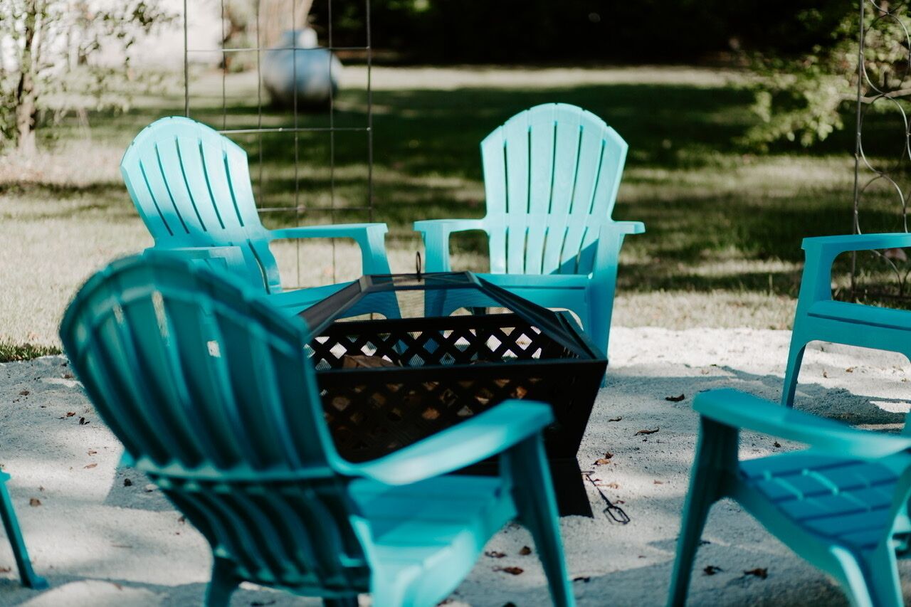 A set of turquoise Adirondack chairs arranged around a black wicker table on a concrete surface.