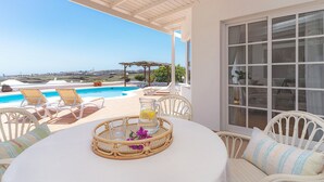 A covered outdoor seating area with a pool view, wicker furniture, and a table with a glass pitcher and flowers. - Amazing 3 bedroom Ocean view with pool (Tías)