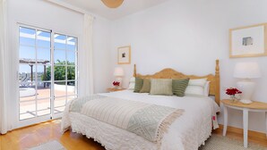 A bedroom with a large bed, two bedside tables with lamps, a window with curtains, and a framed picture on the wall. - Amazing 3 bedroom Ocean view with pool (Tías)