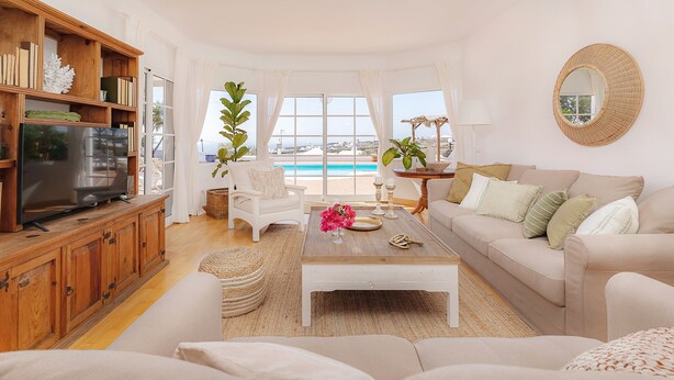 A spacious living room with a large TV, comfortable seating, a coffee table, and a view of a pool. - Amazing 3 bedroom Ocean view with pool (Tías)