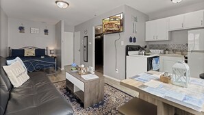 Een modern appartement met een woonkamer, keuken en eethoek. Het heeft een bank, salontafel en een keuken met witte kasten en een koelkast.
