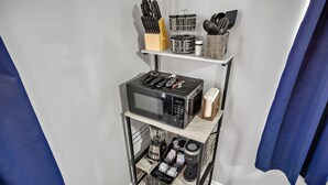 Een keuken met een magnetron, broodrooster en koffiezetapparaat op een plank, en diverse keukengerei op een andere plank.