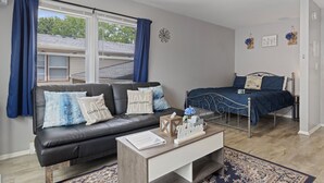 Een moderne slaapkamer met een donker leren bank, een houten salontafel, een metalen bedframe en een blauwe spreidek.