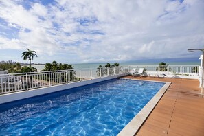 Una piscina con muelle de madera y barandilla blanca, con vista a una playa y al océano.