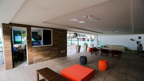 A spacious living area with a wooden bench, orange seating, and a view of the outdoors. - Apart Praia de Cabo Branco por Carpediem (João Pessoa)