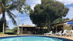 A swimming pool with tiled blue edges, surrounded by palm trees and a building with a tiled roof. - Beautiful, cozy, and well-equipped - Geribá within walking distance! (Armação dos Búzios)
