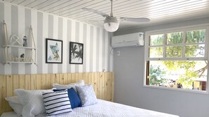 A bedroom with a bed, striped walls, a ceiling fan, a window with a view, and wall-mounted air conditioning. - Beautiful, cozy, and well-equipped - Geribá within walking distance! (Armação dos Búzios)