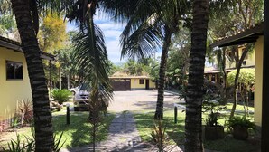 A paved pathway leading to a yellow building with a tiled roof, surrounded by palm trees and greenery. - Beautiful, cozy, and well-equipped - Geribá within walking distance! (Armação dos Búzios)