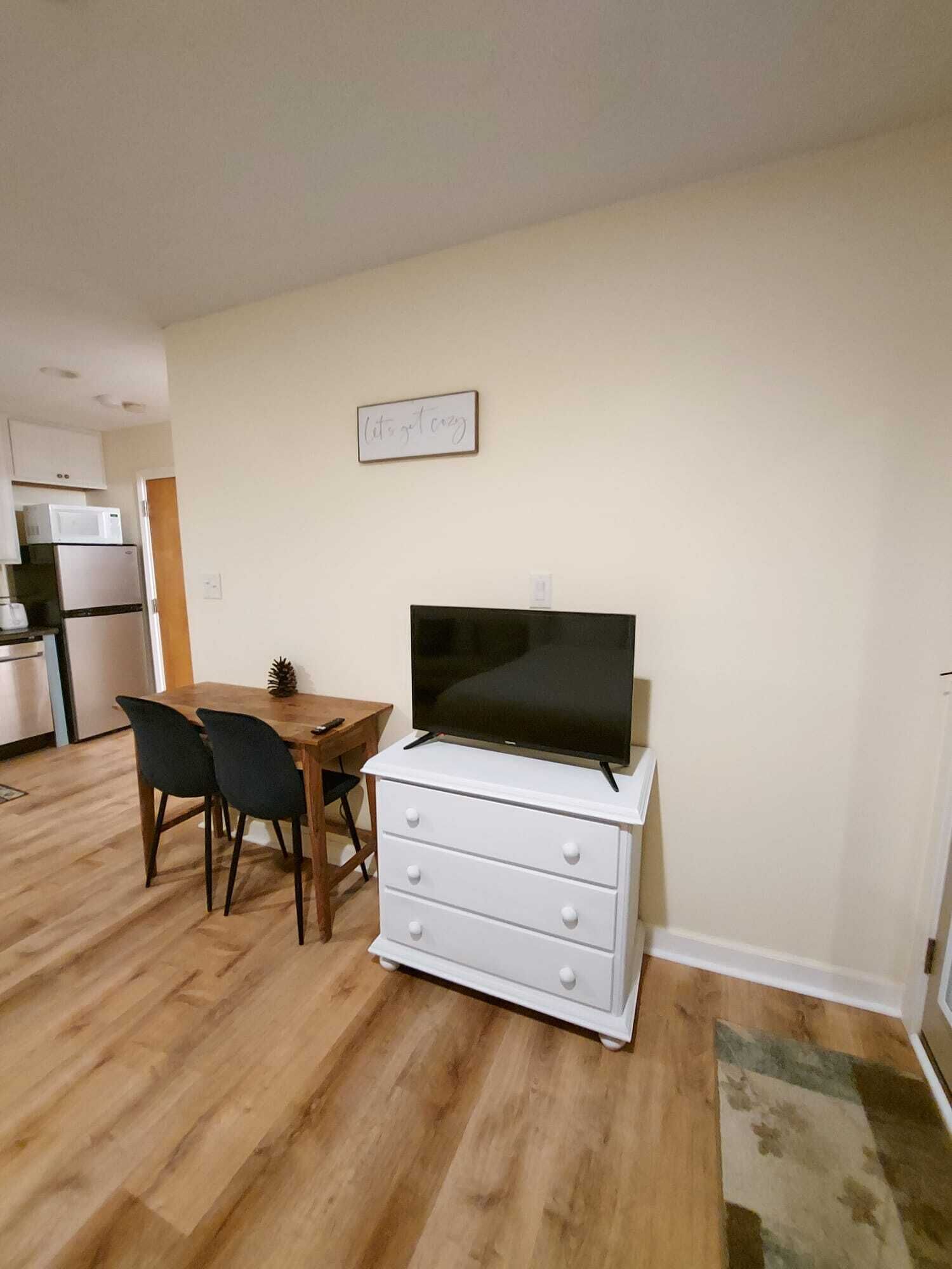 A compact living space with a dining area, a kitchenette, and a television on a dresser.