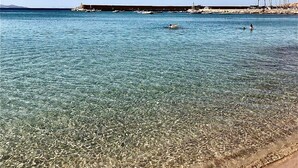 Una spiaggia sabbiosa con vista sul mare aperto, acque calme e un molo in lontananza con imbarcazioni.