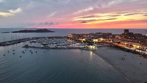 Una cittadina costiera al tramonto con un porto turistico, barche e edifici lungo il lungomare.