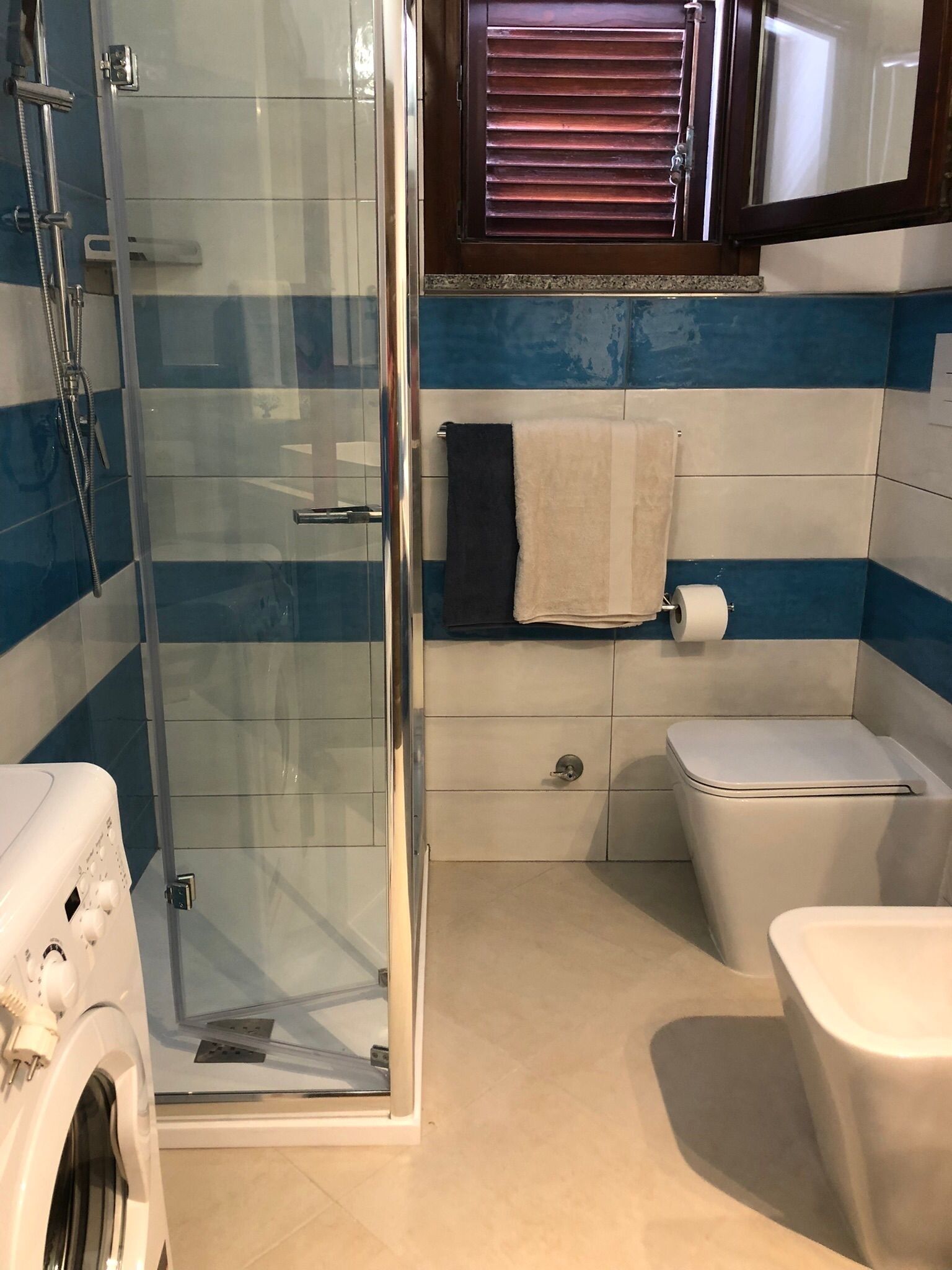 A bathroom with a glass shower enclosure, a toilet, and a washing machine.