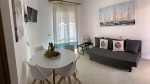 Un soggiorno moderno con zona pranzo, che include un tavolo rotondo con sedie, un divano con cuscini decorativi e un quadro con velieri sulla parete.