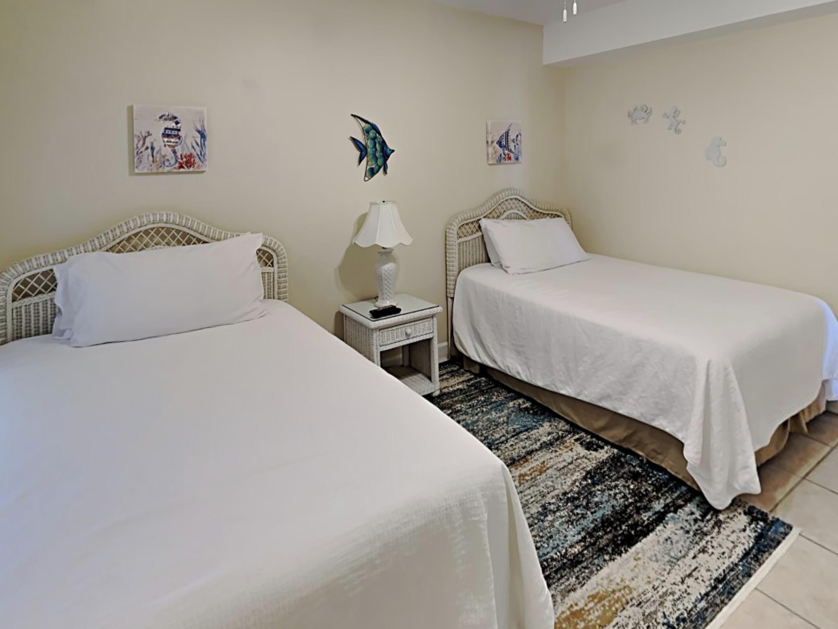 A room with two single beds, a nightstand with a lamp, and a patterned rug.