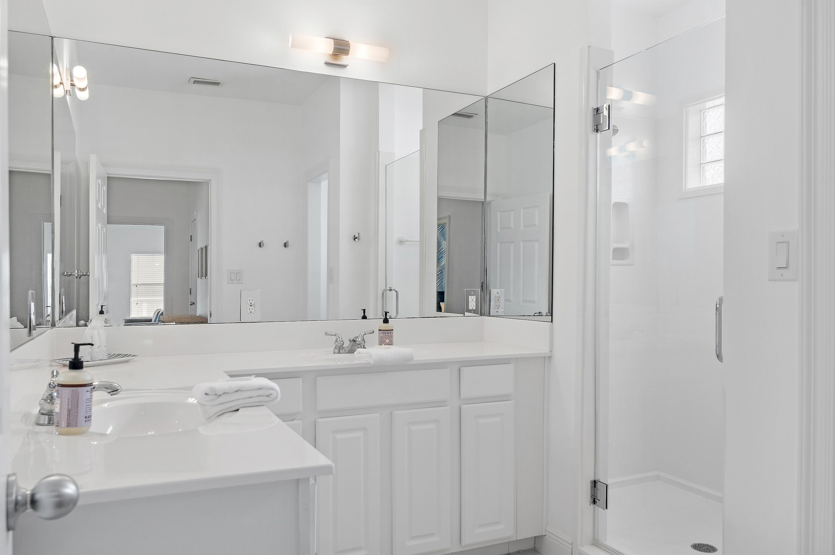 A modern bathroom with a large mirror, white cabinetry, and a shower area.