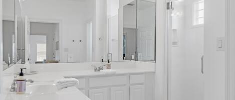 A modern bathroom with a large mirror, white cabinetry, and a shower area.