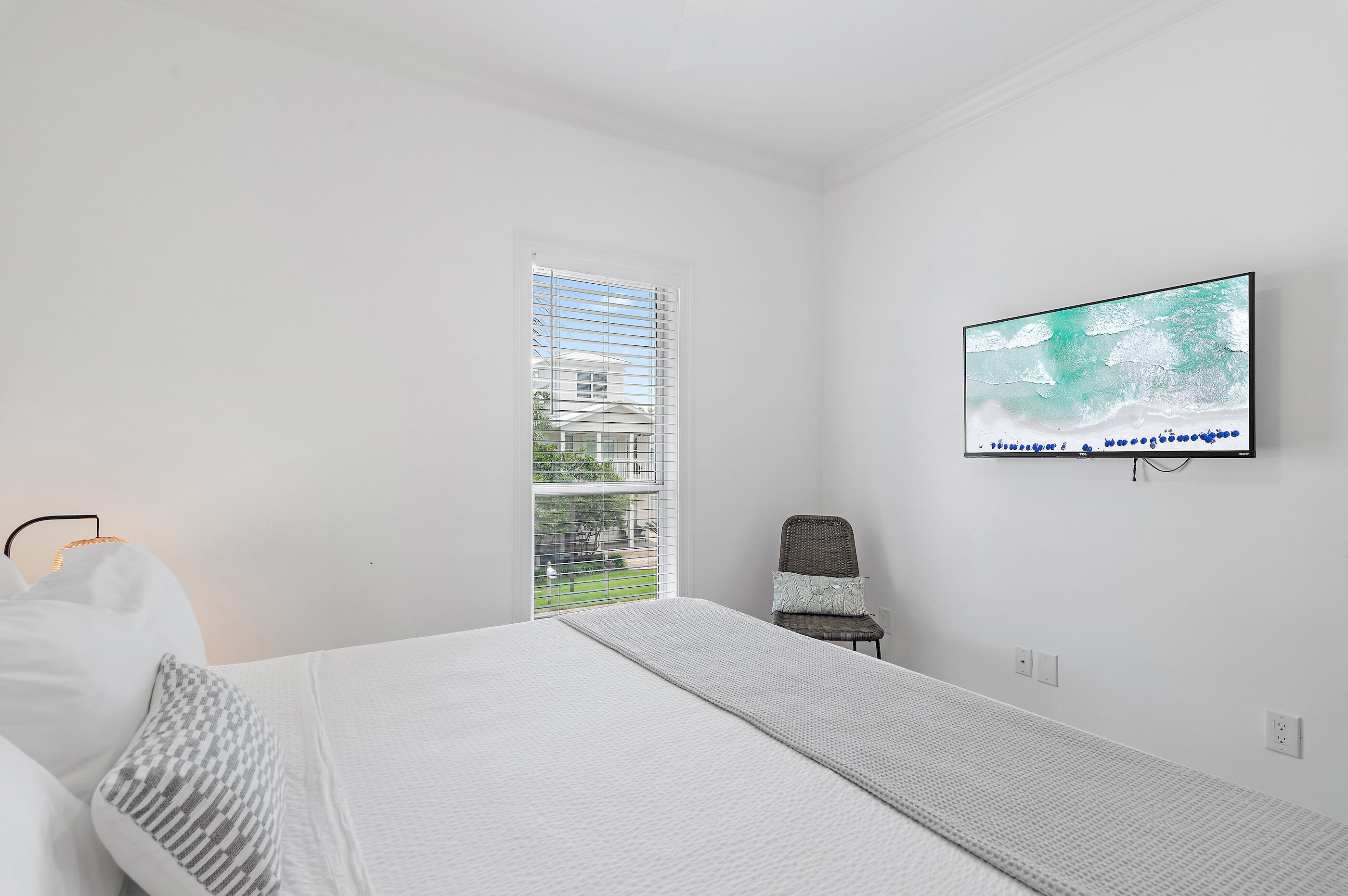 A modern bedroom with a bed, a television mounted on the wall, a window with blinds, and a chair.