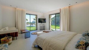 Ein modernes Schlafzimmer mit einem großen Bett, einer Couch, einem Fernseher und Blick ins Freie.