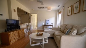Ein Wohnzimmer mit einer Couch, einem Couchtisch, einem Fernseher auf einem Holzschrank, einem Esstisch mit Stühlen und einer Küche im Hintergrund.