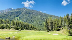 Ein Golfplatz mit Bergblick, einem Teich und blauem Himmel.