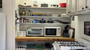 Une cuisine avec des meubles blancs, un four à micro-ondes, un grille-pain et une cuisinière. On y trouve des étagères remplies de divers ustensiles de cuisine et un plan de travail en bois.