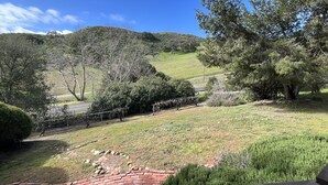 Un jardin aménagé avec un sentier en briques, une terrasse en bois et une vue sur des collines verdoyantes et des arbres.