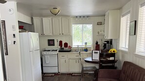 Une cuisine compacte avec des meubles blancs, un réfrigérateur, une cuisinière et un coin repas comprenant une table et des chaises.