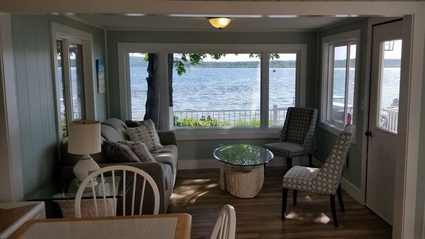 A cozy room with a view of a lake, a glass coffee table, a sofa, and patterned chairs.