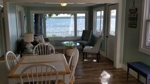 A dining area with a table and chairs, a small round table with a glass top, and a view of a lake through large windows.