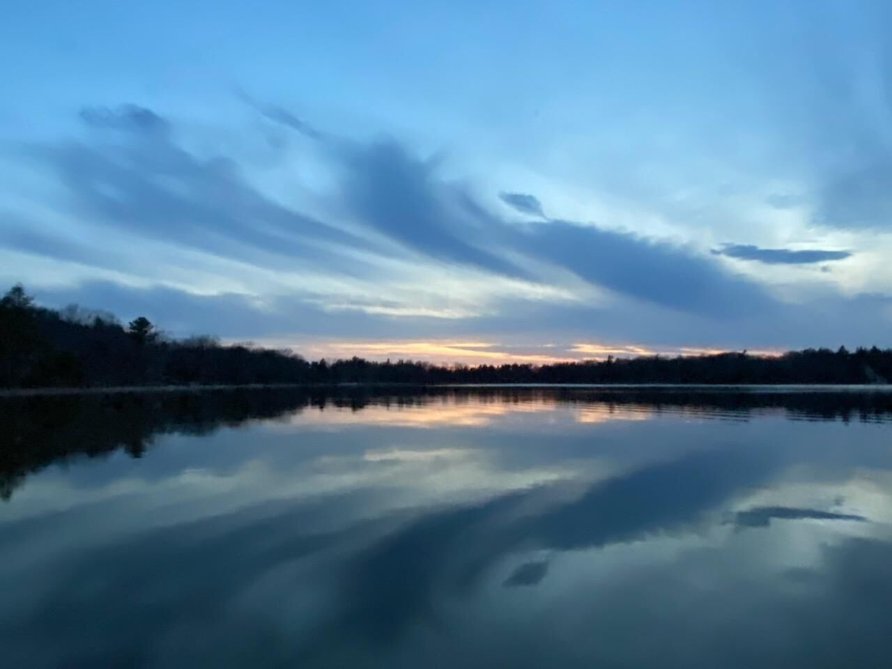 A calm lake at dusk with a clear reflection of the sky and trees.