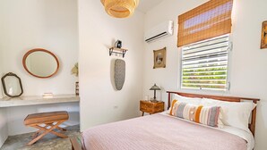 A bedroom with a bed, bedside table, lamp, and a window with blinds.