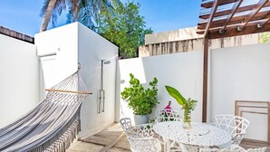 A hammock, white outdoor furniture, and potted plants on a wooden deck.