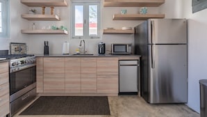 A modern kitchen with wooden cabinets, stainless steel appliances, and floating shelves.
