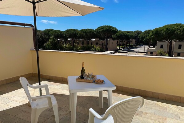 A balcony with a table set for two, a bottle of wine, and snacks.