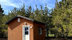 Une petite cabane en bois avec une porte et des fenêtres, une table de pique-nique et un sol recouvert de gravier.