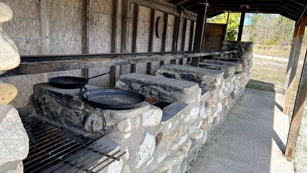 Un espace de cuisson extérieur en pierre, équipé de barbecues et de plats en grès.
