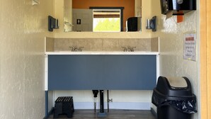 Un couloir étroit avec un lavabo, un miroir, une poubelle et un téléviseur fixé au mur.