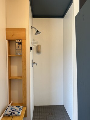 A small, enclosed shower area with a wooden shelf unit containing a box and a small table.