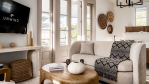 A living room with a sofa, a coffee table, a TV, and a large window. - Villa Rosé - Private pool near Rosemary Beach (Rosemary Beach)