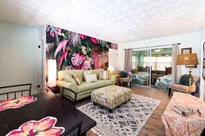 A cozy living room with a green sofa, a dining table, and a tropical-themed wall mural.