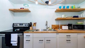 A kitchen with a stove, oven, sink, and wooden shelves above.