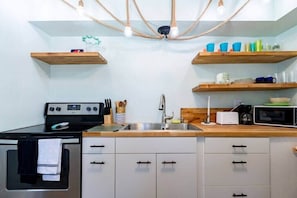 A modern kitchen with a stove, sink, and wooden shelves above.