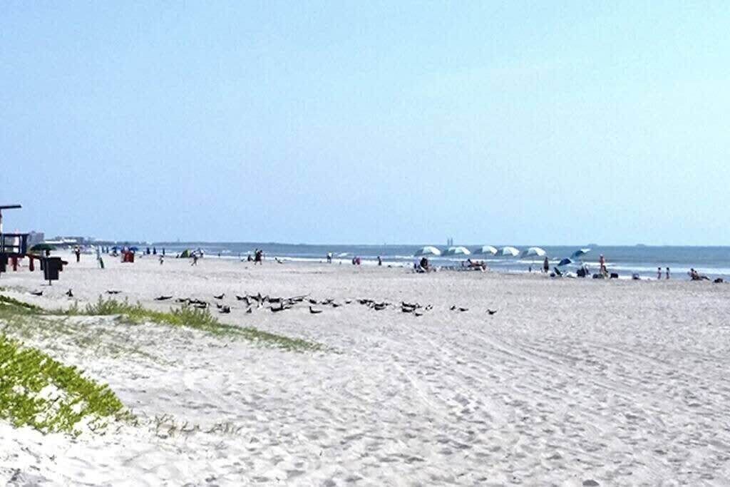 A beach with people and umbrellas, a lifeguard tower, and a distant view of the ocean.
