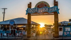 The entrance to Cocoa Beach Pier with a sign indicating it offers restaurants, bars, shops, and fishing.