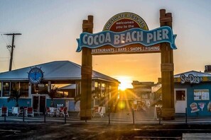 The entrance to Cocoa Beach Pier with a sign indicating it offers restaurants, bars, shops, and fishing.
