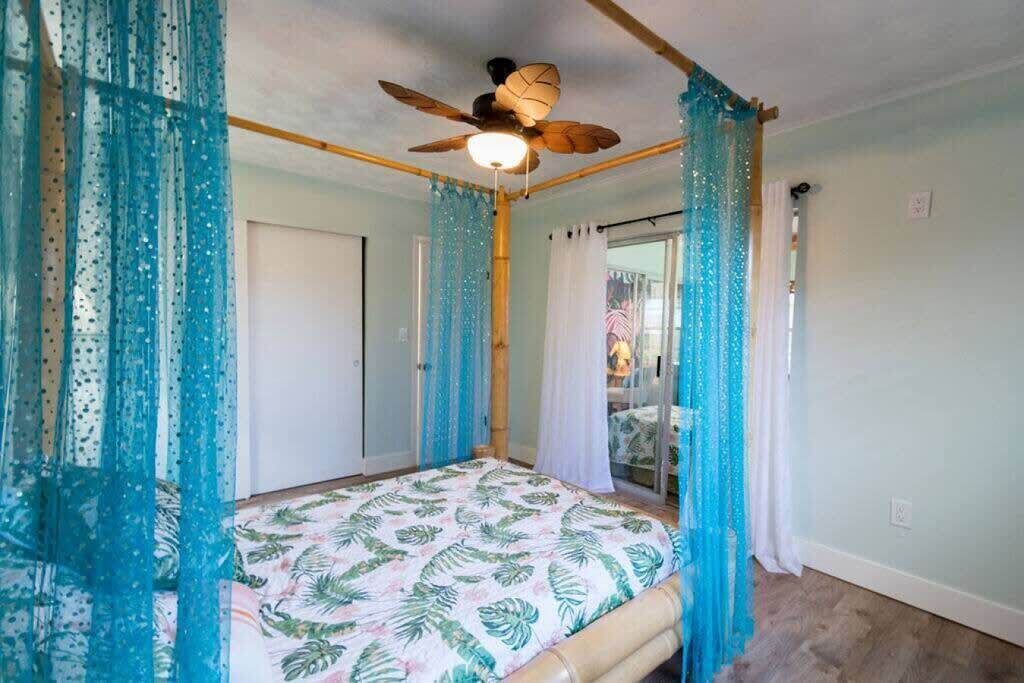 A bedroom with a bed, a ceiling fan, and sheer curtains.